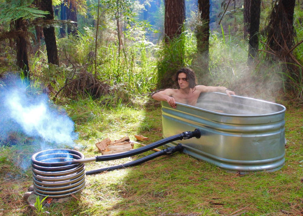Man relaxing in a steaming stock tank hot tub heated by a wood-fired coil in the forest