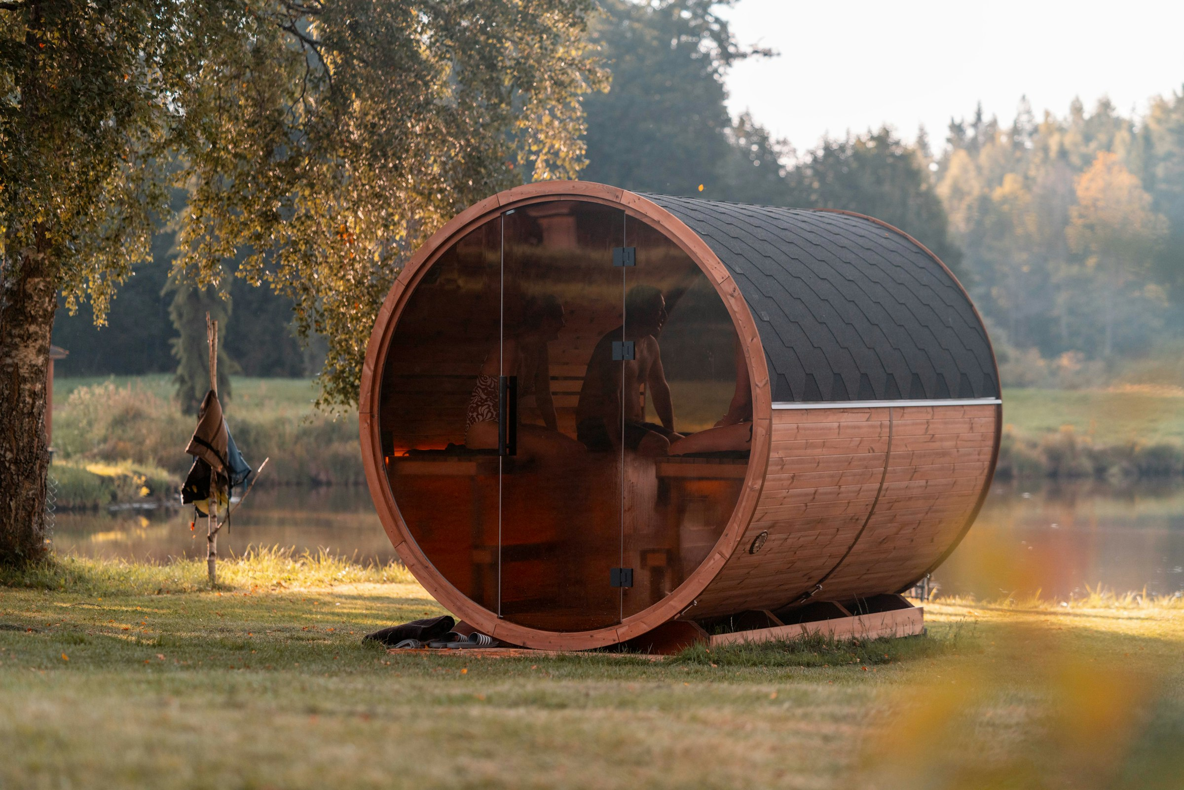 Sauna de barril con frente de vidrio junto a un lago al atardecer