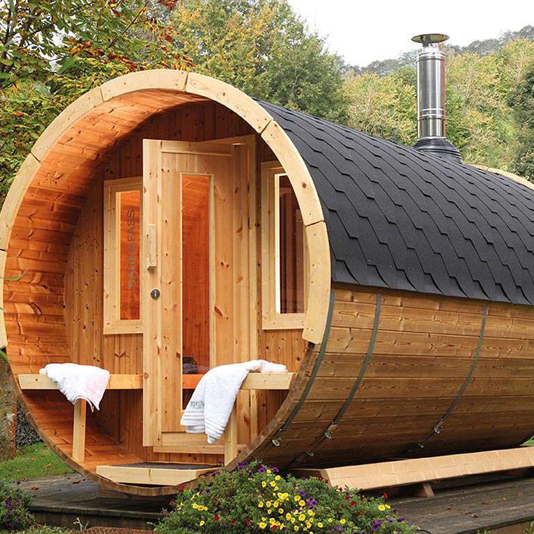 Sauna de barril con terraza techada y chimenea en un jardín